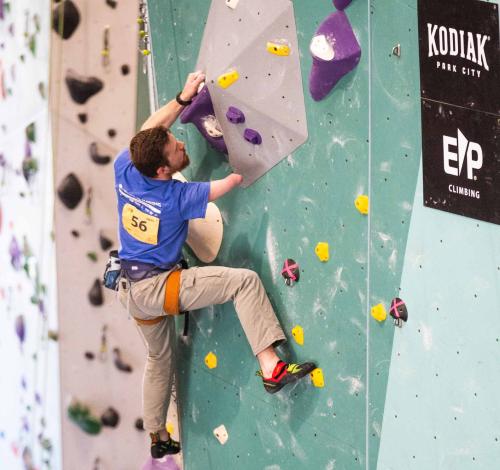 A man without his right arm at the elbow climbs up a rock wall