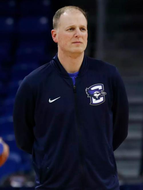 A basketball coach stands with his hands behind his back