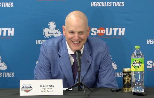 A basketball coach smiles during a post-game press conference