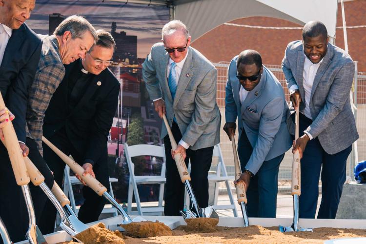 A group of people put shovels into dirt