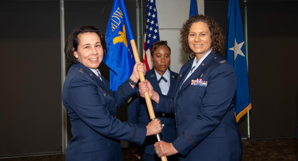 With her two hands on a flag pole, Kristen Nichols smiles in a picture with her commander