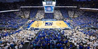 A full basketball arena where fans wear blue and white shirts based on their seating section