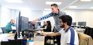 A teacher and student look at a computer monitor.