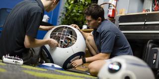 Two male students tinker with a robot