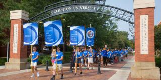 A crowd of students wearing Creighton blue walk under the Creighton arch.
