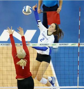 Volleyball player Norah Sis attacking at the net.