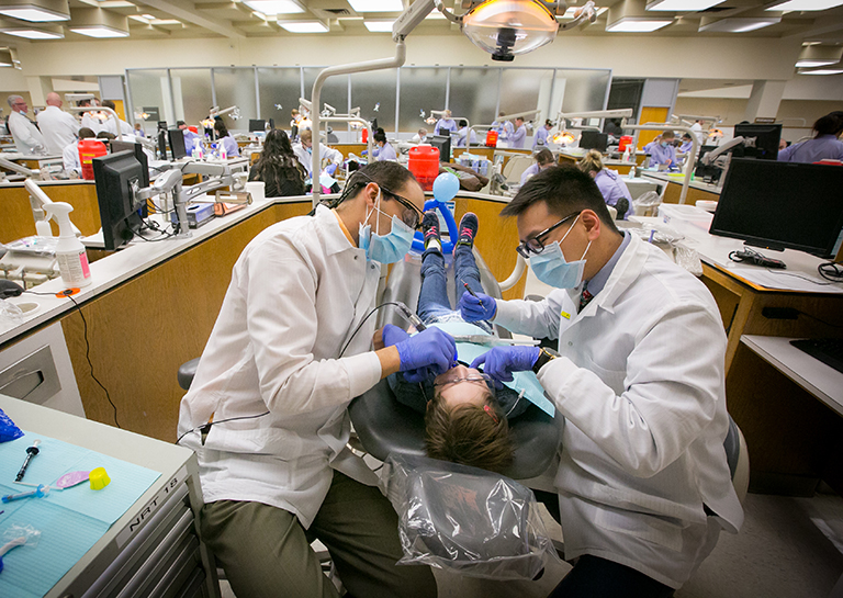 Two dental students provide care to a patient in the dental clinic