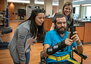 PT students work with a patient while he shows them something on his phone.